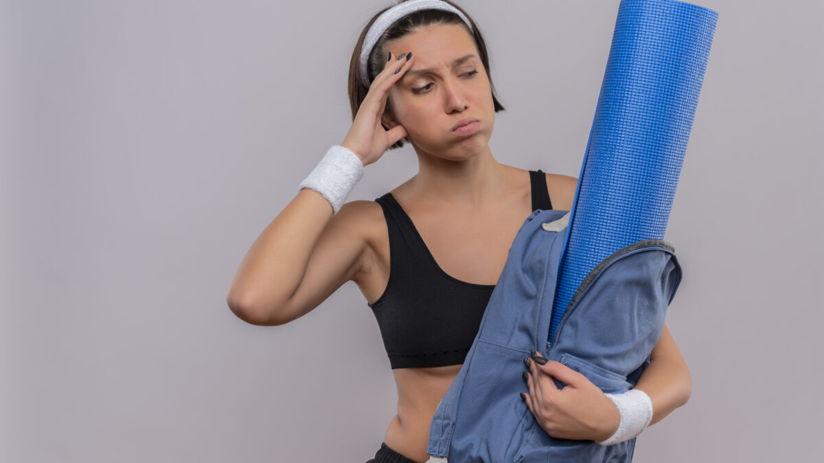 Mulher confusa e cansada segurando mochila com colchonete de yoga.