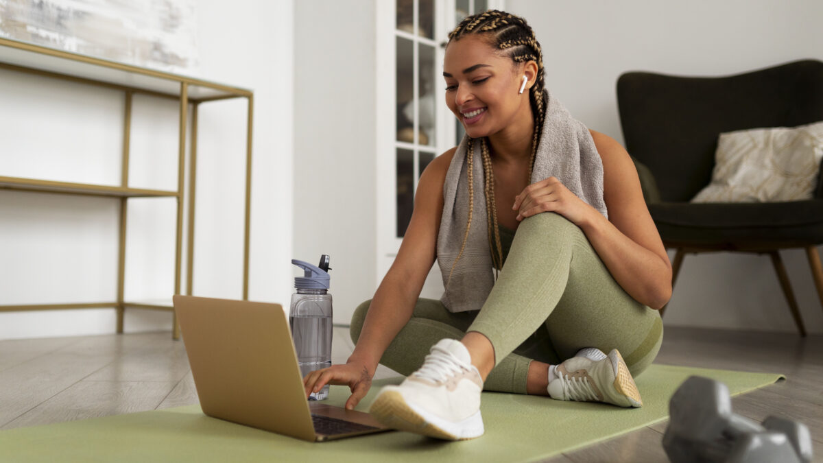 Mulher praticando exercício físico com notebook em casa, unindo movimento e produtividade no trabalho remoto.