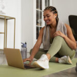 Mulher praticando exercício físico com notebook em casa, unindo movimento e produtividade no trabalho remoto.