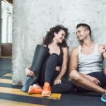 Casal aproveita momento de descontração na academia após um treino em dupla, reforçando os benefícios da parceria nos exercícios.