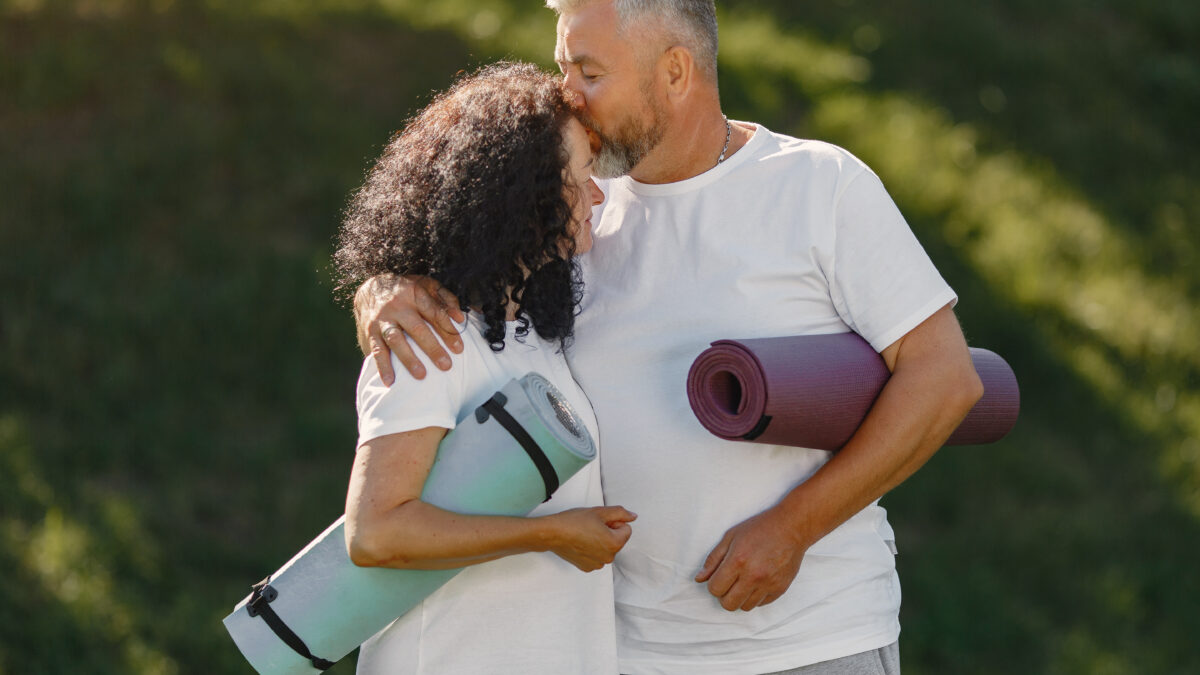 Casal sênior praticando ioga ao ar livre, simbolizando a conexão entre saúde sexual e exercício para qualidade de vida.
