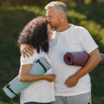Casal sênior praticando ioga ao ar livre, simbolizando a conexão entre saúde sexual e exercício para qualidade de vida.