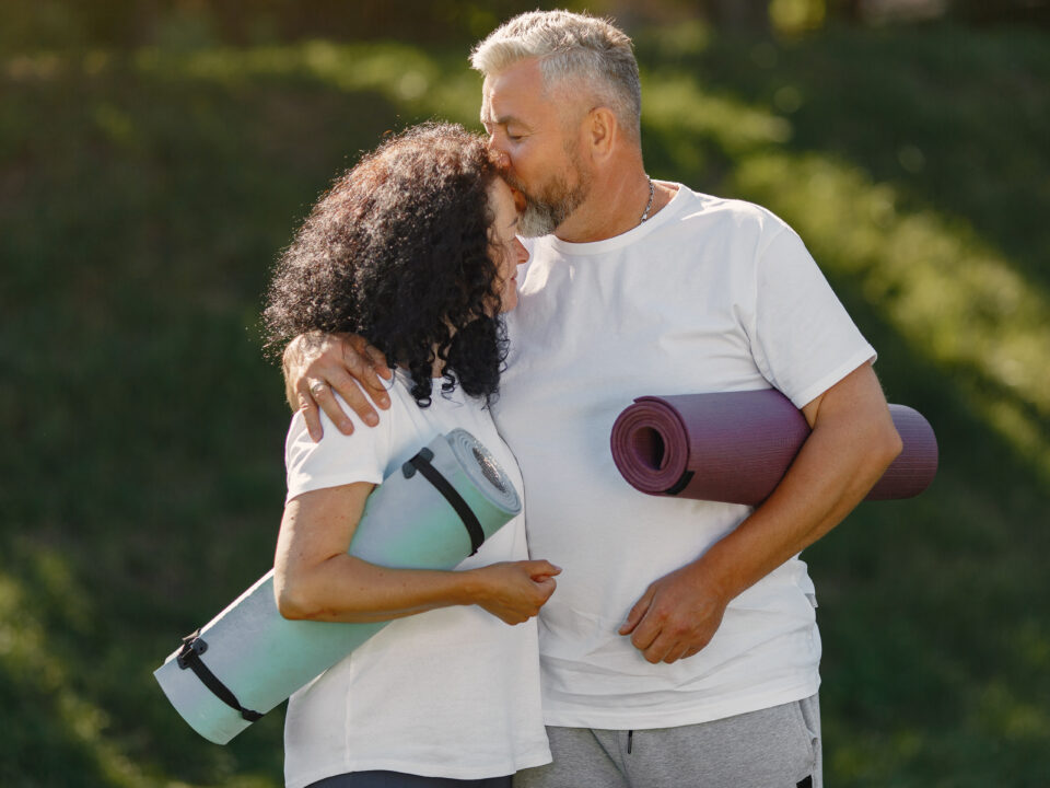 Casal sênior praticando ioga ao ar livre, simbolizando a conexão entre saúde sexual e exercício para qualidade de vida.